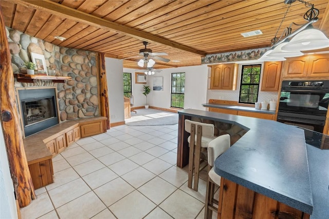 kitchen with a healthy amount of sunlight, wooden ceiling, a fireplace, light tile patterned floors, and dobule oven black