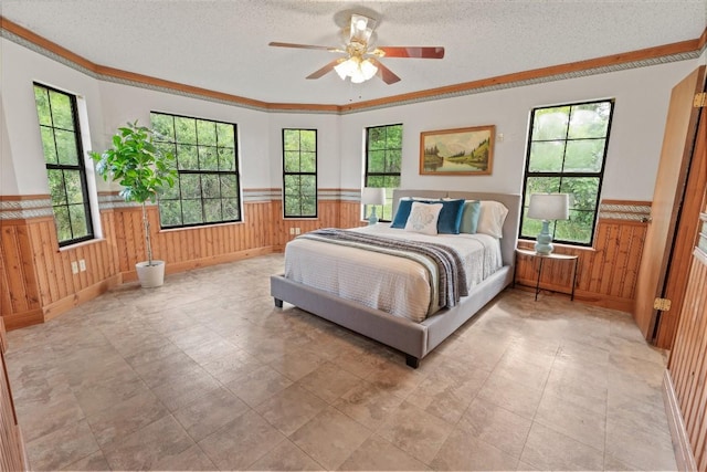 bedroom with a textured ceiling, multiple windows, wood walls, and a wainscoted wall