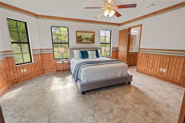 bedroom featuring wooden walls, crown molding, wainscoting, and visible vents