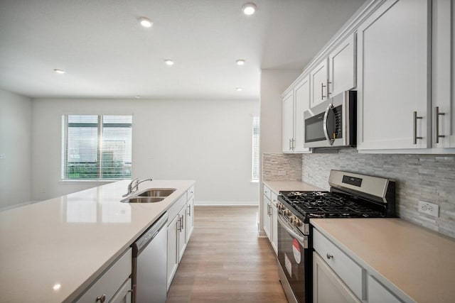 kitchen featuring a sink, appliances with stainless steel finishes, light countertops, decorative backsplash, and light wood-style floors