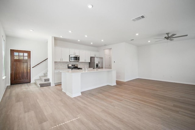kitchen with stainless steel appliances, light wood-type flooring, visible vents, an island with sink, and open floor plan