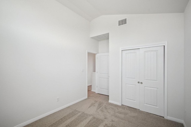 unfurnished bedroom featuring a closet, visible vents, baseboards, light colored carpet, and lofted ceiling