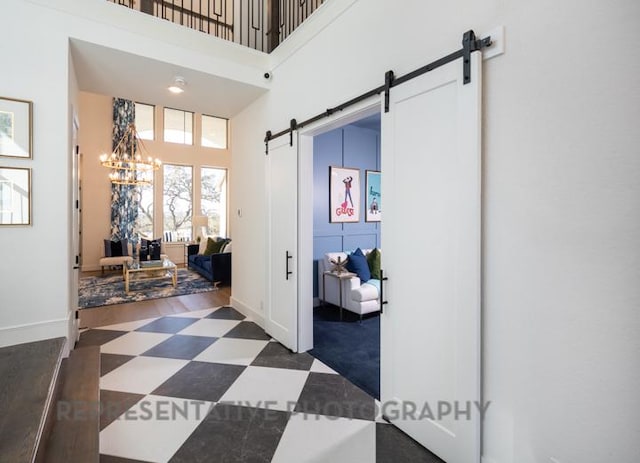 hall featuring a barn door, baseboards, an inviting chandelier, tile patterned floors, and a high ceiling