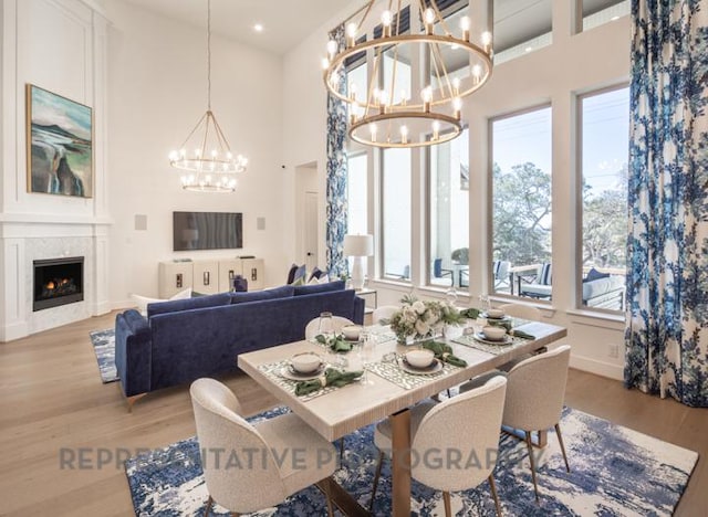 dining area with an inviting chandelier, a towering ceiling, a wealth of natural light, and light wood finished floors