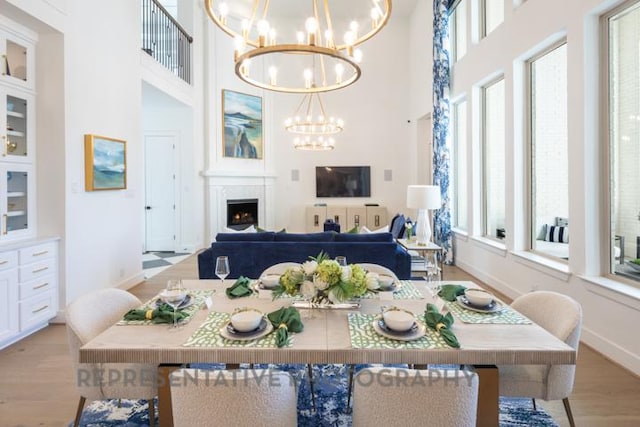 dining space featuring light wood-style flooring, baseboards, an inviting chandelier, a lit fireplace, and a towering ceiling