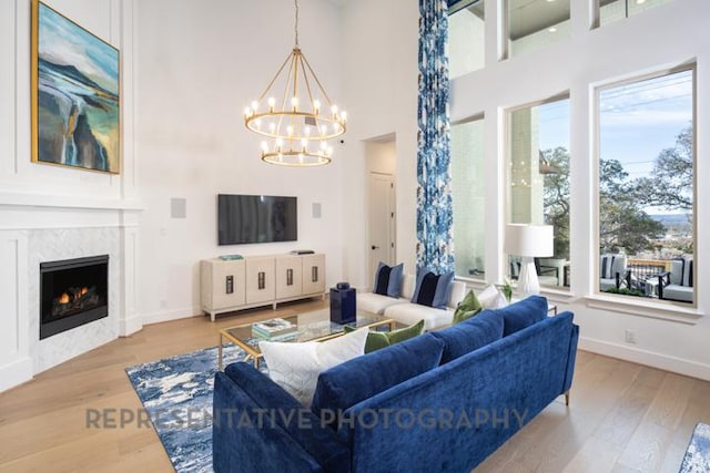 living room featuring wood finished floors, a premium fireplace, a notable chandelier, baseboards, and a towering ceiling