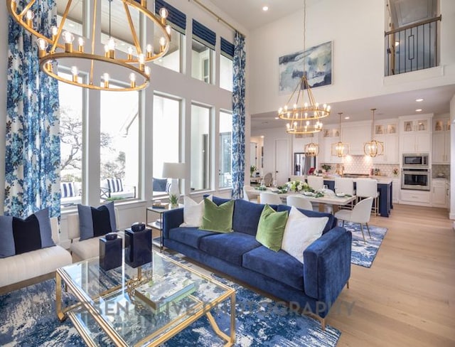 living area featuring an inviting chandelier, light wood-type flooring, a towering ceiling, and recessed lighting