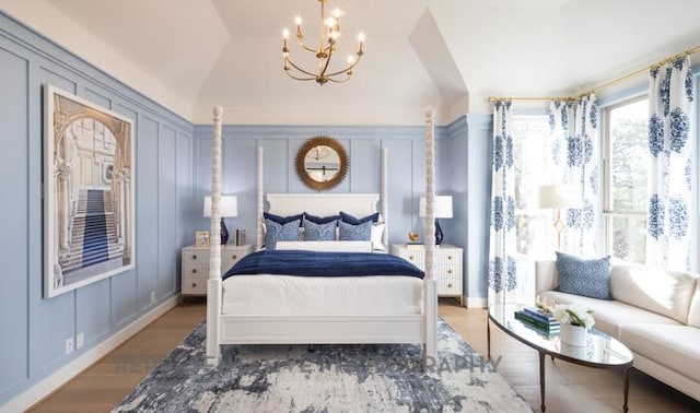 bedroom featuring vaulted ceiling, a notable chandelier, a decorative wall, and wood finished floors