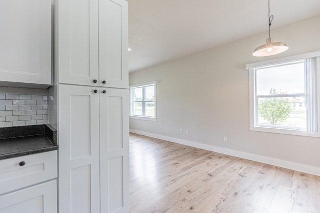 kitchen featuring backsplash, dark countertops, baseboards, and light wood-style floors