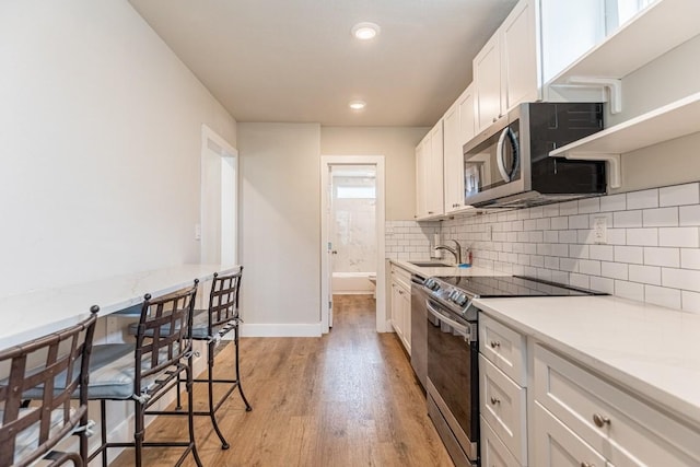 kitchen with light wood-style flooring, a sink, backsplash, stainless steel appliances, and white cabinets