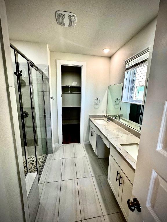 4319 Port Hope St, Round Rock, TX 78665 - bathroom featuring a stall shower, double vanity, a walk in closet, a textured ceiling, and tile patterned floors
