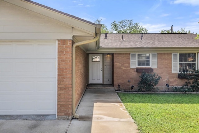doorway to property with a yard, a shingled roof, brick siding, and a garage