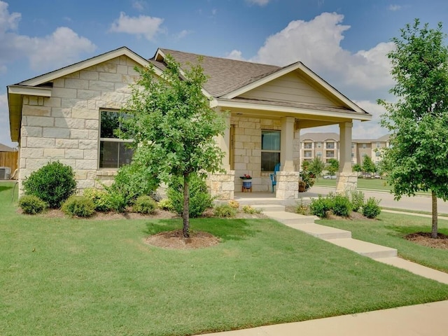 view of front of property with stone siding, covered porch, central AC unit, a front yard, and roof with shingles