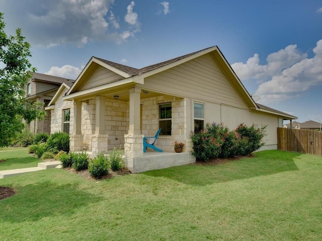 view of property exterior featuring a yard, stone siding, covered porch, and fence