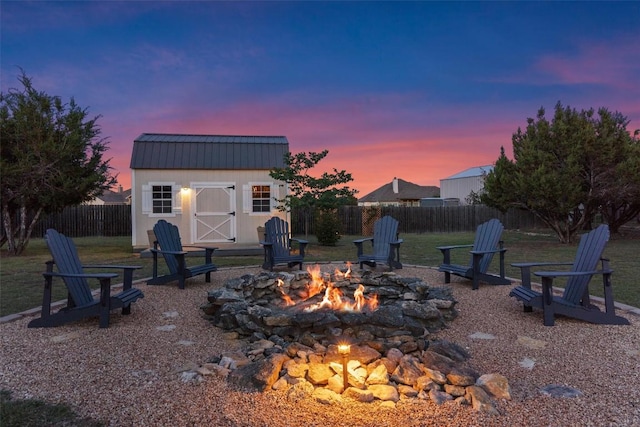 yard at dusk with an outdoor fire pit, an outdoor structure, a fenced backyard, and a storage unit
