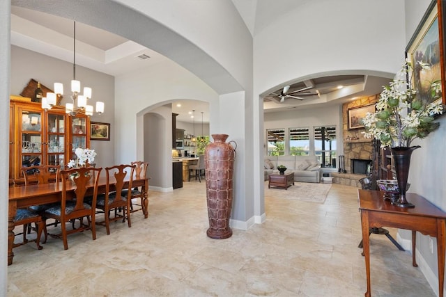 interior space with a tray ceiling, a stone fireplace, ceiling fan with notable chandelier, arched walkways, and a high ceiling