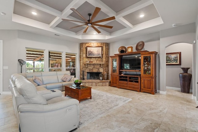 living room featuring coffered ceiling, baseboards, a stone fireplace, ceiling fan, and arched walkways