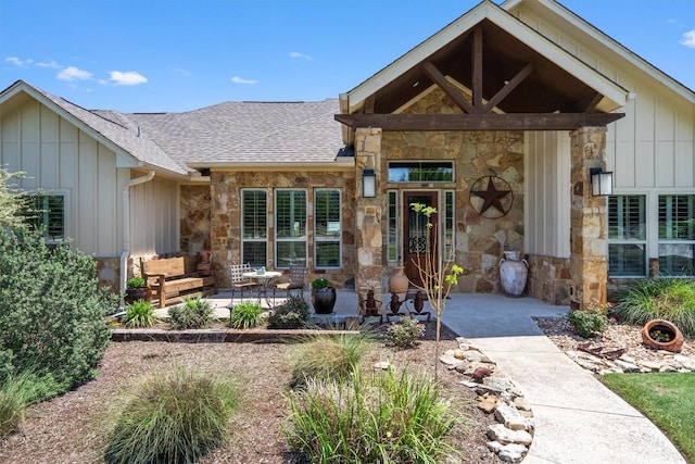 view of front facade featuring stone siding, board and batten siding, a patio area, and roof with shingles