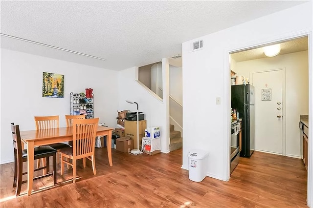 dining area featuring stairway, a textured ceiling, visible vents, and wood finished floors