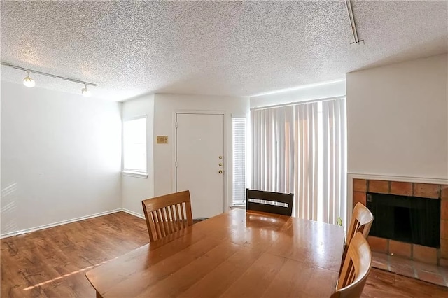 unfurnished dining area with rail lighting, a textured ceiling, a tiled fireplace, and wood finished floors