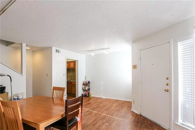 dining space featuring wood finished floors, rail lighting, a textured ceiling, visible vents, and baseboards