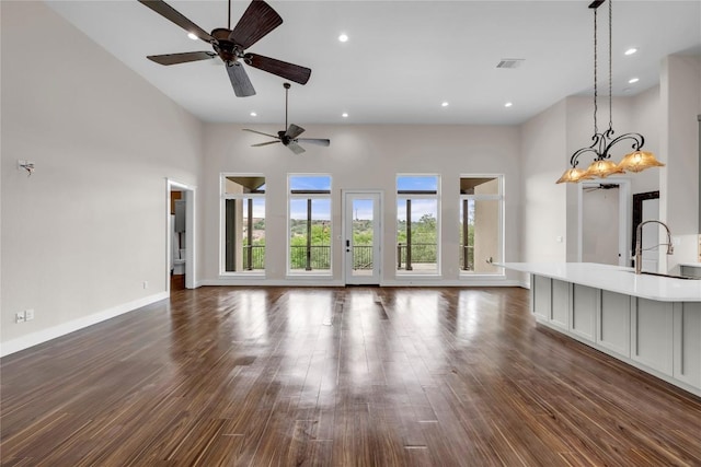 unfurnished living room with baseboards, dark wood-style flooring, a towering ceiling, and ceiling fan with notable chandelier