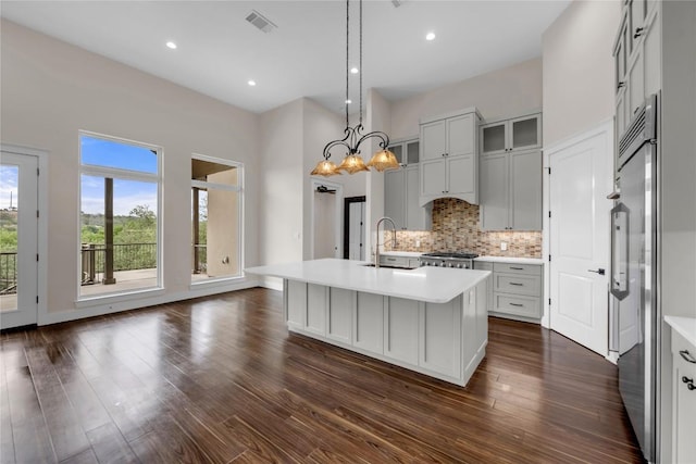 kitchen featuring stainless steel built in refrigerator, an island with sink, light countertops, and visible vents