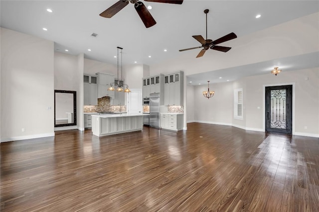 unfurnished living room with visible vents, ceiling fan with notable chandelier, a high ceiling, and dark wood-style floors