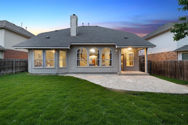 back of house featuring a chimney, a shingled roof, a fenced backyard, a yard, and a patio area