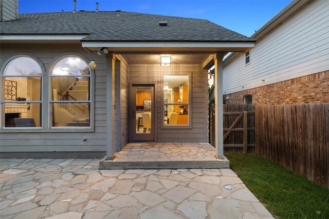 view of exterior entry with a shingled roof and fence