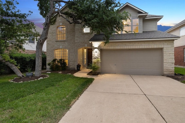 traditional-style house with an attached garage, stone siding, concrete driveway, a front lawn, and roof with shingles