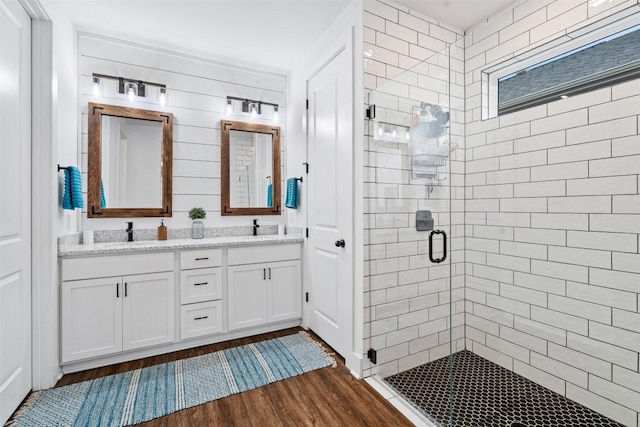 full bath with double vanity, wood finished floors, a stall shower, and a sink