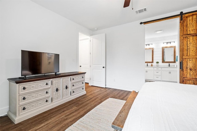bedroom featuring visible vents, a barn door, baseboards, dark wood-type flooring, and ensuite bath