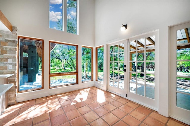 unfurnished sunroom with tile patterned floors, a wealth of natural light, french doors, and a high ceiling