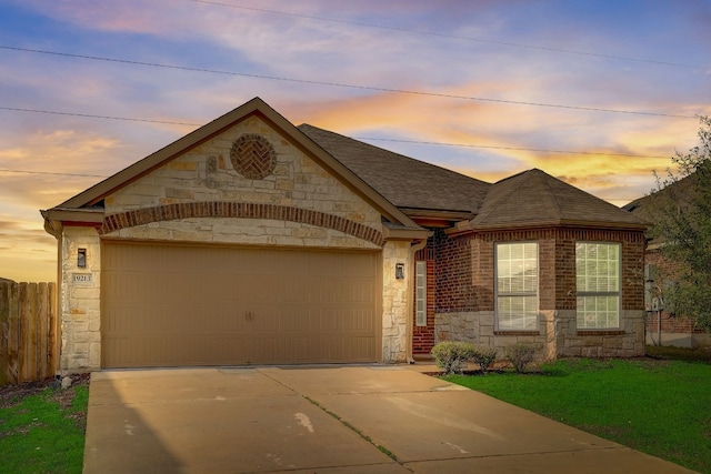 view of front of house with stone siding, a garage, a shingled roof, a yard, and driveway