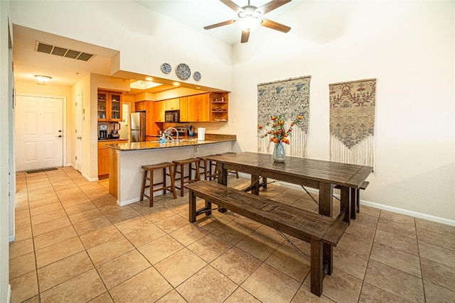 dining space featuring a towering ceiling, visible vents, a ceiling fan, light tile patterned floors, and baseboards