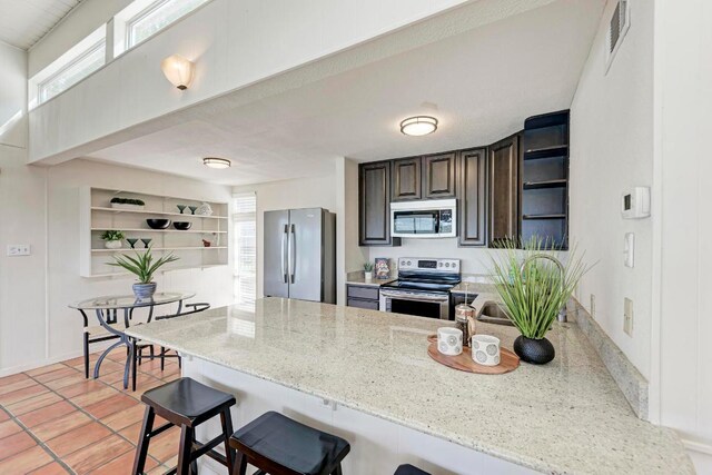 8130 Joy Rd, Volente, TX 78641 - kitchen with a peninsula, open shelves, a breakfast bar area, light stone countertops, and appliances with stainless steel finishes