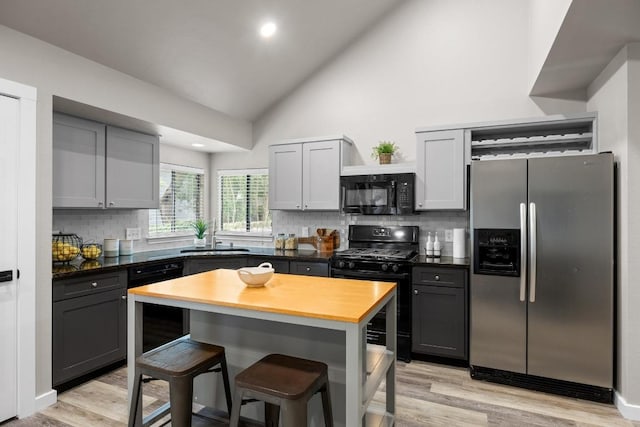 13105 Lubbock Ln, Austin, TX 78729 - kitchen featuring black appliances, a kitchen bar, gray cabinets, light wood-type flooring, and backsplash