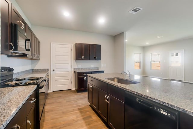 kitchen with a sink, light stone counters, black appliances, recessed lighting, and light wood-style floors