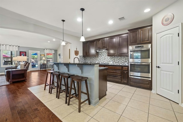 152 Florenz Ln, Georgetown, TX 78628 - kitchen featuring visible vents, open floor plan, a kitchen breakfast bar, dark countertops, and double oven