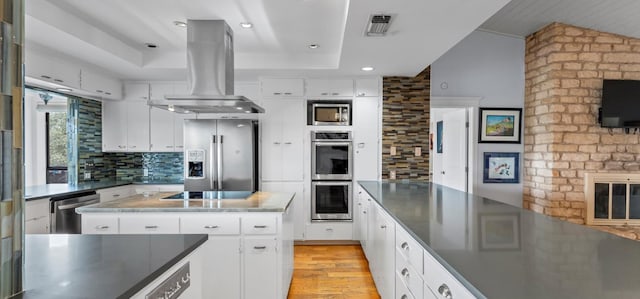 6714 Mtn Trl, Austin, TX 78732 - kitchen with appliances with stainless steel finishes, island range hood, a tray ceiling, backsplash, and light wood-style floors