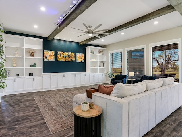 living area featuring a ceiling fan, a healthy amount of sunlight, dark wood finished floors, and beam ceiling