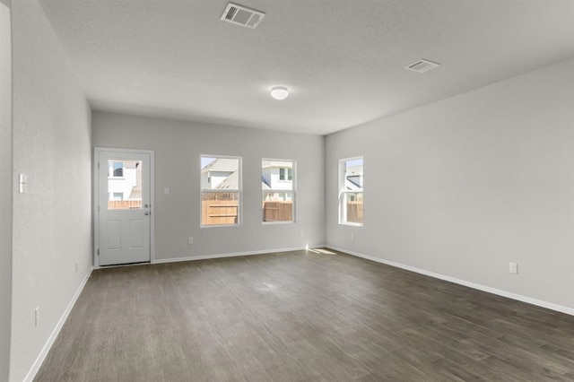 unfurnished room with visible vents, a healthy amount of sunlight, and dark wood-style floors