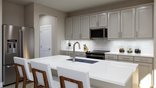 kitchen featuring a sink, tasteful backsplash, light countertops, appliances with stainless steel finishes, and gray cabinetry