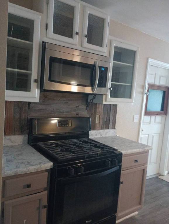8730 Meadow Song, Converse, TX 78109 - kitchen with black gas range, stainless steel microwave, glass insert cabinets, and dark wood-style flooring