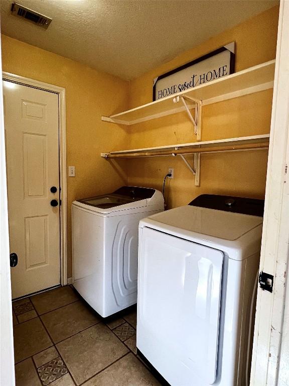 clothes washing area featuring laundry area, a textured ceiling, visible vents, tile patterned floors, and washing machine and dryer