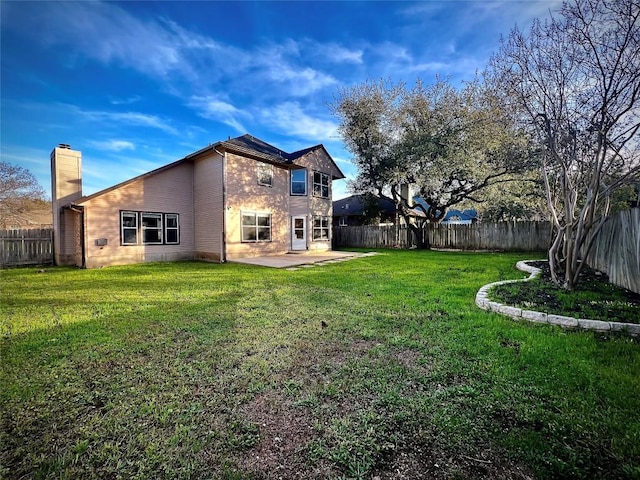 back of house featuring a chimney, a yard, a patio, and a fenced backyard