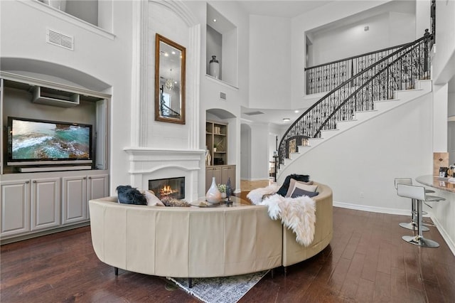 living room featuring stairway, a high ceiling, dark wood-style floors, and a glass covered fireplace