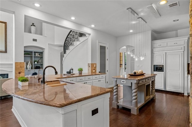 kitchen with dark wood finished floors, visible vents, a sink, arched walkways, and a large island with sink