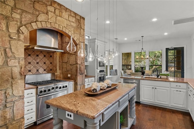 kitchen featuring a sink, stainless steel appliances, wall chimney range hood, backsplash, and a kitchen island